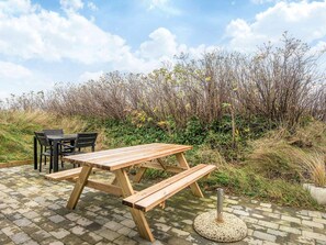 An outdoor wooden picnic table with benches, a metal pole, and a brick-paved area.