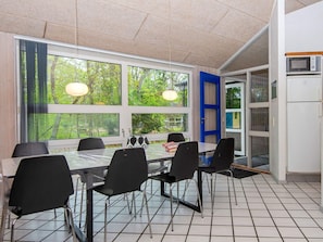 A dining area with a table and chairs, large windows, and a door leading to a kitchen. - 5 Star Holiday Home in Glesborg (Glesborg)