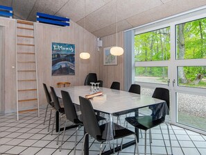 A dining area with a large table, chairs, and a view of greenery through large windows. - 5 Star Holiday Home in Glesborg (Glesborg)