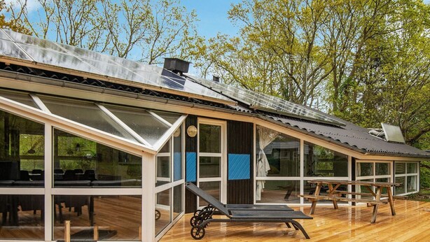 Una casa moderna con amplios ventanales, una terraza de madera y un panel solar en el techo.