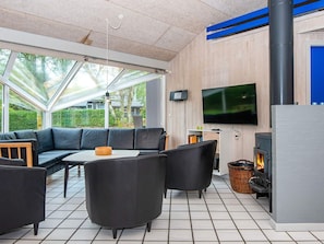 A modern outdoor living space with a glass-enclosed area, a black leather sofa, a dining table, and a fireplace. - 5 Star Holiday Home in Glesborg (Glesborg)