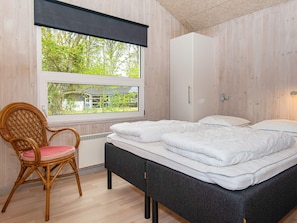 Une chambre à coucher comprenant un lit, une chaise, une armoire et une fenêtre donnant sur un paysage verdoyant.