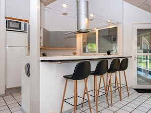 A modern kitchen with a central island, bar stools, a microwave, and a stainless steel range hood. - 5 Star Holiday Home in Glesborg (Glesborg)