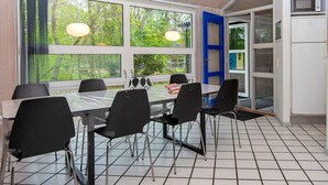 Un comedor con una mesa, sillas y ventanas amplias con vistas a árboles.
