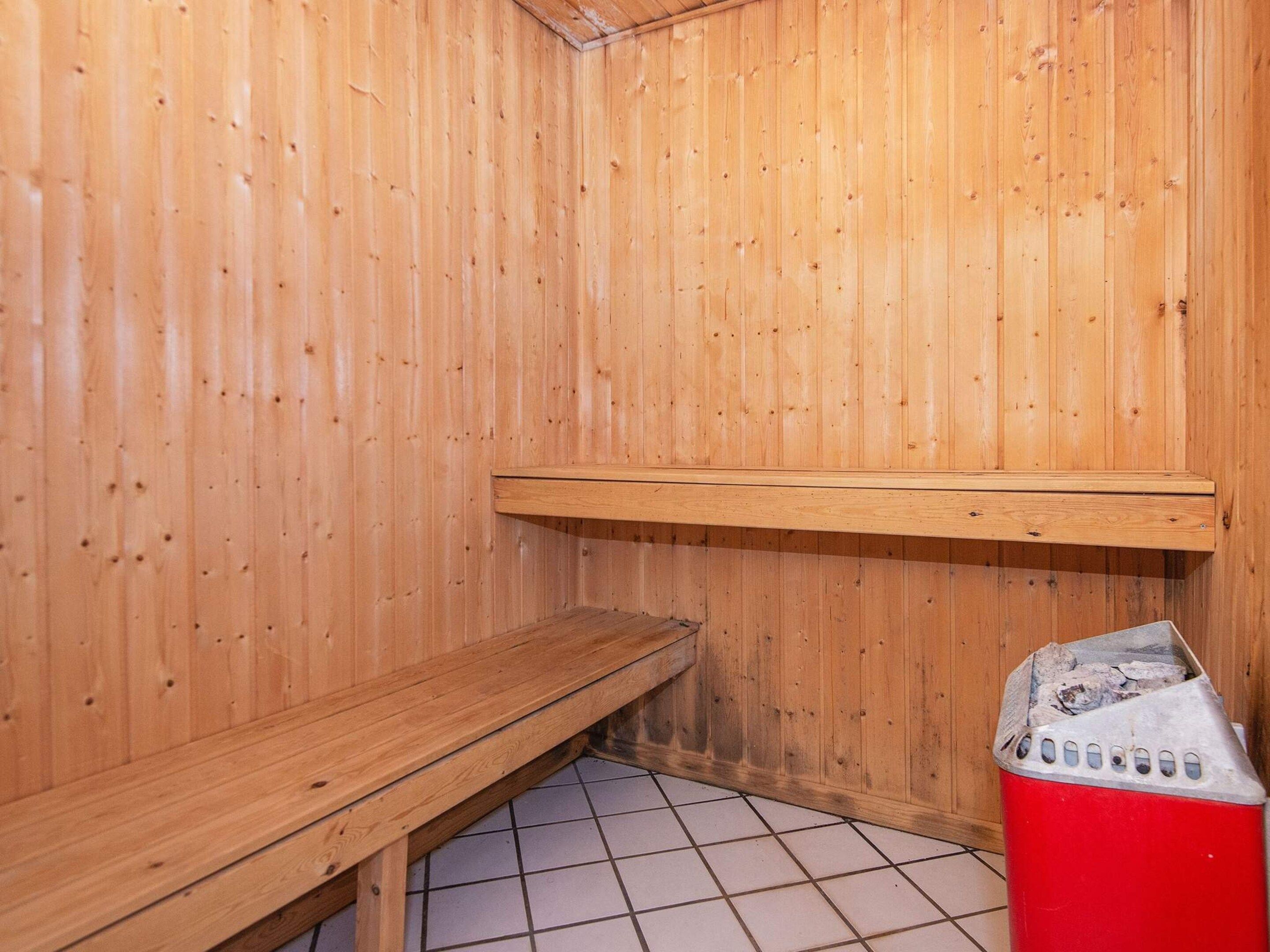 Una sala de sauna con paredes de madera, un banco y un cubo de basura rojo.