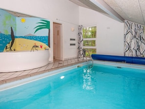 A swimming pool with a mural of a beach scene, a jacuzzi, and a window with a view of greenery. - 5 Star Holiday Home in Glesborg (Glesborg)