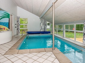 Une piscine intérieure avec de l’eau bleue, un jacuzzi blanc et une vue sur l’extérieur.