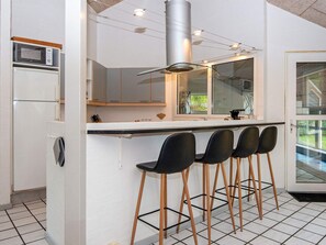 A modern kitchen with a central island, bar stools, a microwave, and a stainless steel range hood. - 5 Star Holiday Home in Glesborg (Glesborg)