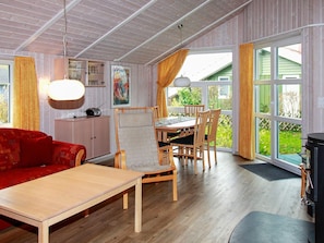 Et værelse med et træbord, stole, en sofa, et skab og et stort vindue med gardiner.