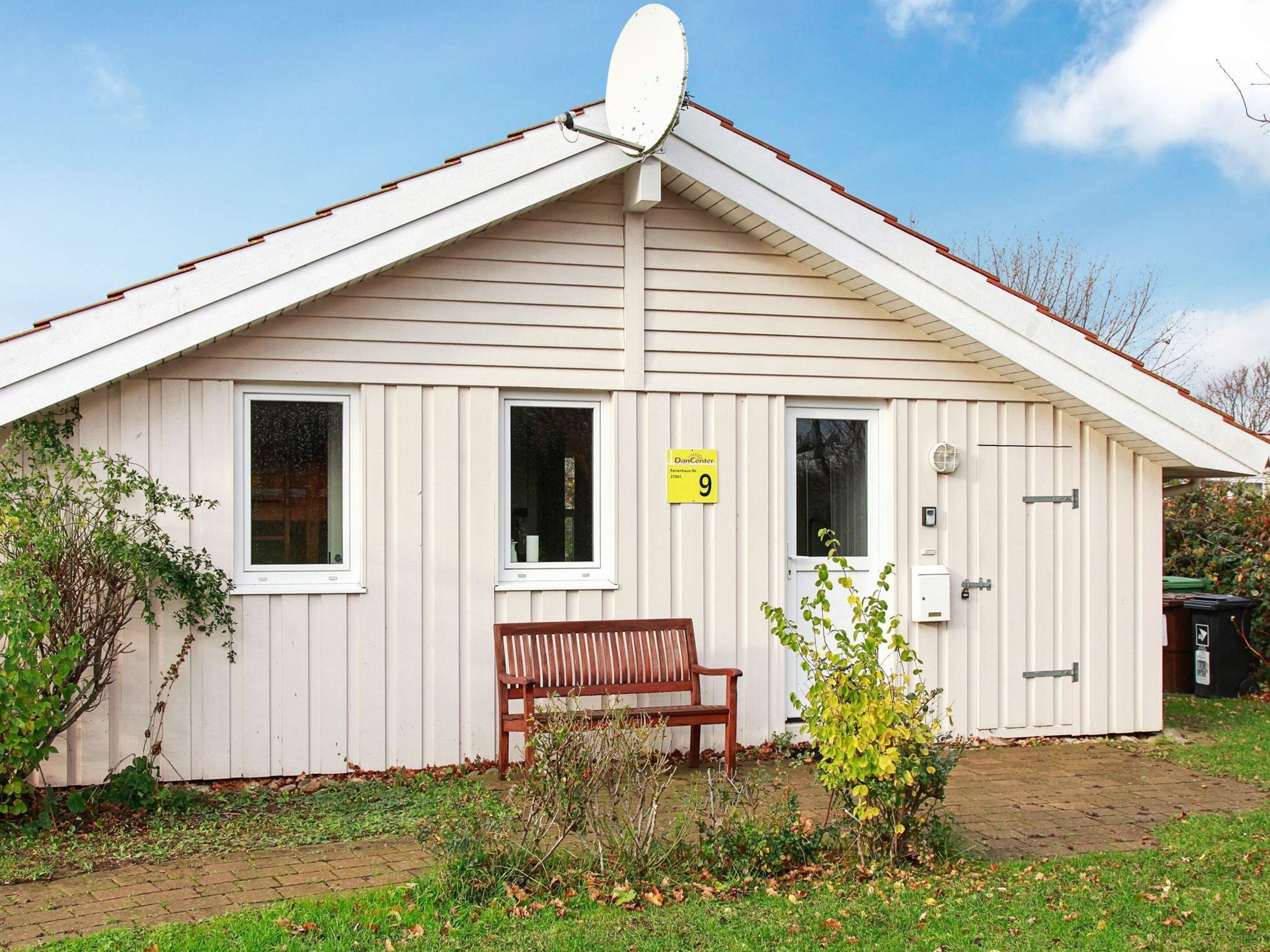 A small, single-story building with a sloped roof, a bench outside, and a door with a number sign.