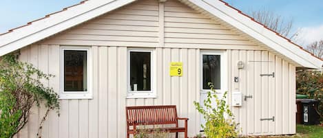 A small, single-story building with a sloped roof, a bench outside, and a door with a number sign.