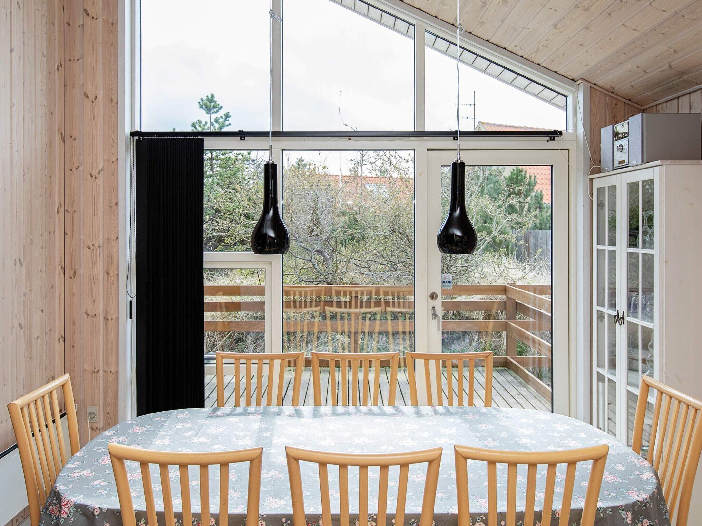 Un comedor con una mesa redonda, sillas de madera y lámparas colgantes negras.