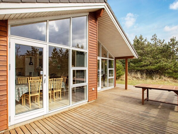 A wooden deck with a dining area and large windows.