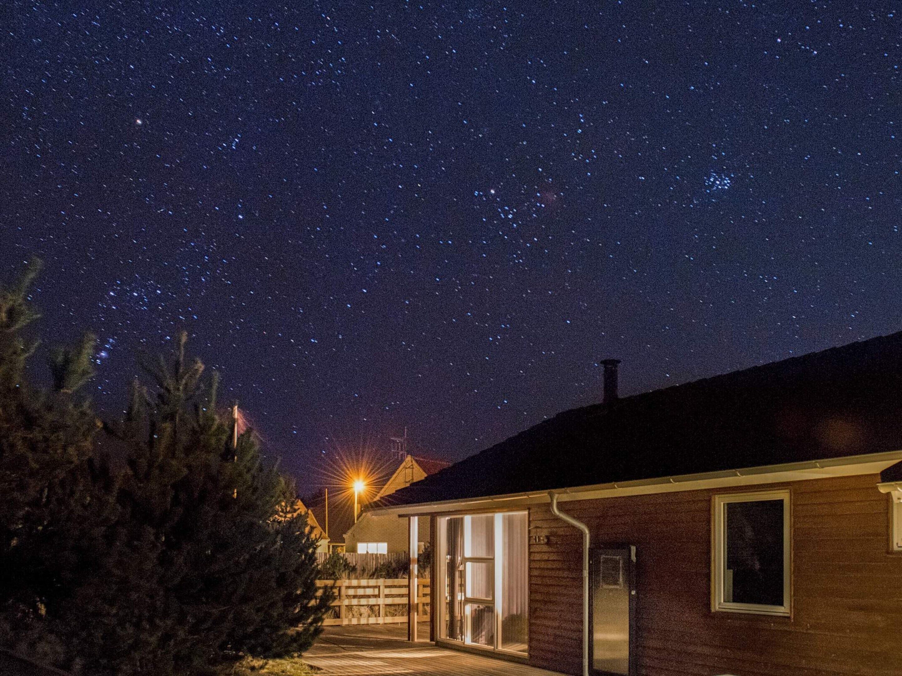 Une maison sous un ciel nocturne dégagé, avec une cheminée bien visible et une entrée bien éclairée.