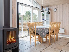 A dining area with a wood-burning stove, wooden chairs, a table with a floral tablecloth, and a view through glass doors.