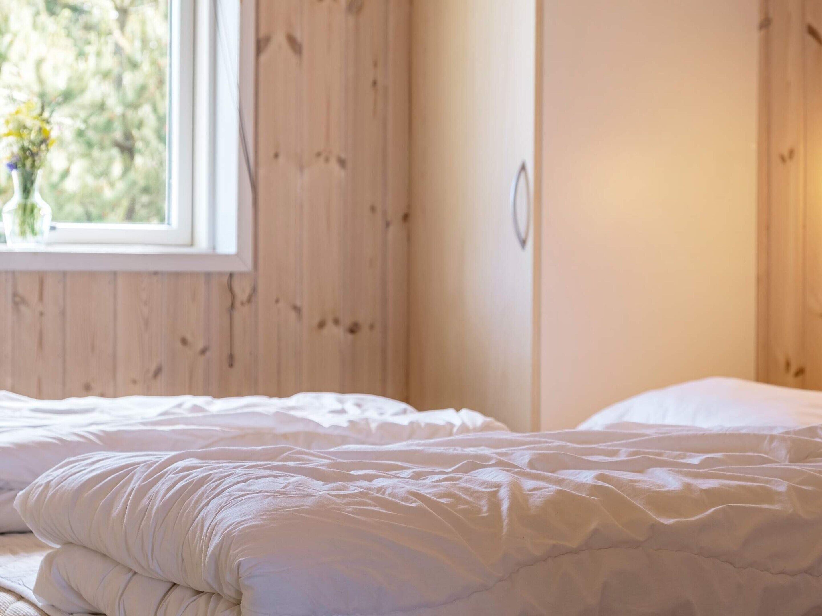 A bedroom with a bed, wooden walls, and a window with a view of greenery.