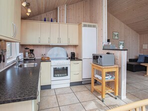 A modern kitchen with wooden cabinets, a stove, a microwave, and a small table with a kettle.