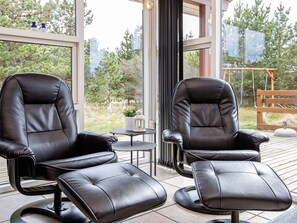 Dos sillones de cuero negro en una terraza de madera, con vista a árboles y un columpio al fondo.