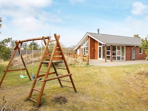A wooden swing set and a house with a tiled roof and large windows.