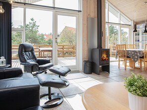 A modern living room with a fireplace, leather chairs, a dining table, and a view through large windows.