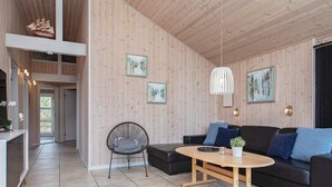 En moderne stue med træloft, en sort sofa med blå puder, et rundt træbord og en sort metalstol.