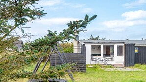 A small, single-story cabin with a patio area, a wooden deck, and a fenced garden. - 6 Person Holiday Home in Harboore (Harboore)