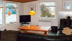 A cozy living room with a wooden ceiling, a black leather sofa, a wooden coffee table, a television, and a fireplace. - 6 Person Holiday Home in Harboore (Harboore)