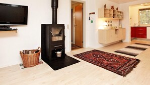 Un salon avec un poêle à bois noir, un téléviseur à écran plat, un panier en osier et un tapis à motifs.