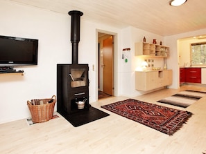 A living room with a black wood-burning stove, a flat-screen TV, a wicker basket, and a patterned rug. - 6 Person Holiday Home in Millinge (Millinge)