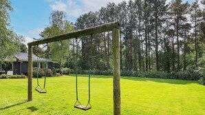Un ensemble de balançoires en bois installé dans une cour verdoyante, avec une maison en arrière-plan.