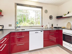 A modern kitchen with red cabinetry, a Siemens dishwasher, a stove, and a window with a view of trees. - 6 Person Holiday Home in Millinge (Millinge)