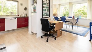 Une cuisine moderne avec des meubles rouges, un lave-vaisselle blanc et un coin repas comprenant une table en bois et des chaises bleues.