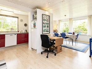 Una cocina moderna con armarios rojos, un lavavajillas blanco y una zona de comedor con mesa de madera y sillas azules.