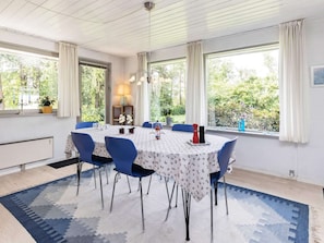 A dining area with a table set for four, blue chairs, a patterned tablecloth, and a view of greenery outside. - 6 Person Holiday Home in Millinge (Millinge)