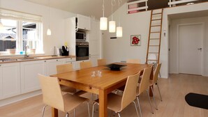 A modern kitchen with white cabinets, a dining table with chairs, and pendant lighting. - 5 Star Holiday Home in Nysted (Nysted)