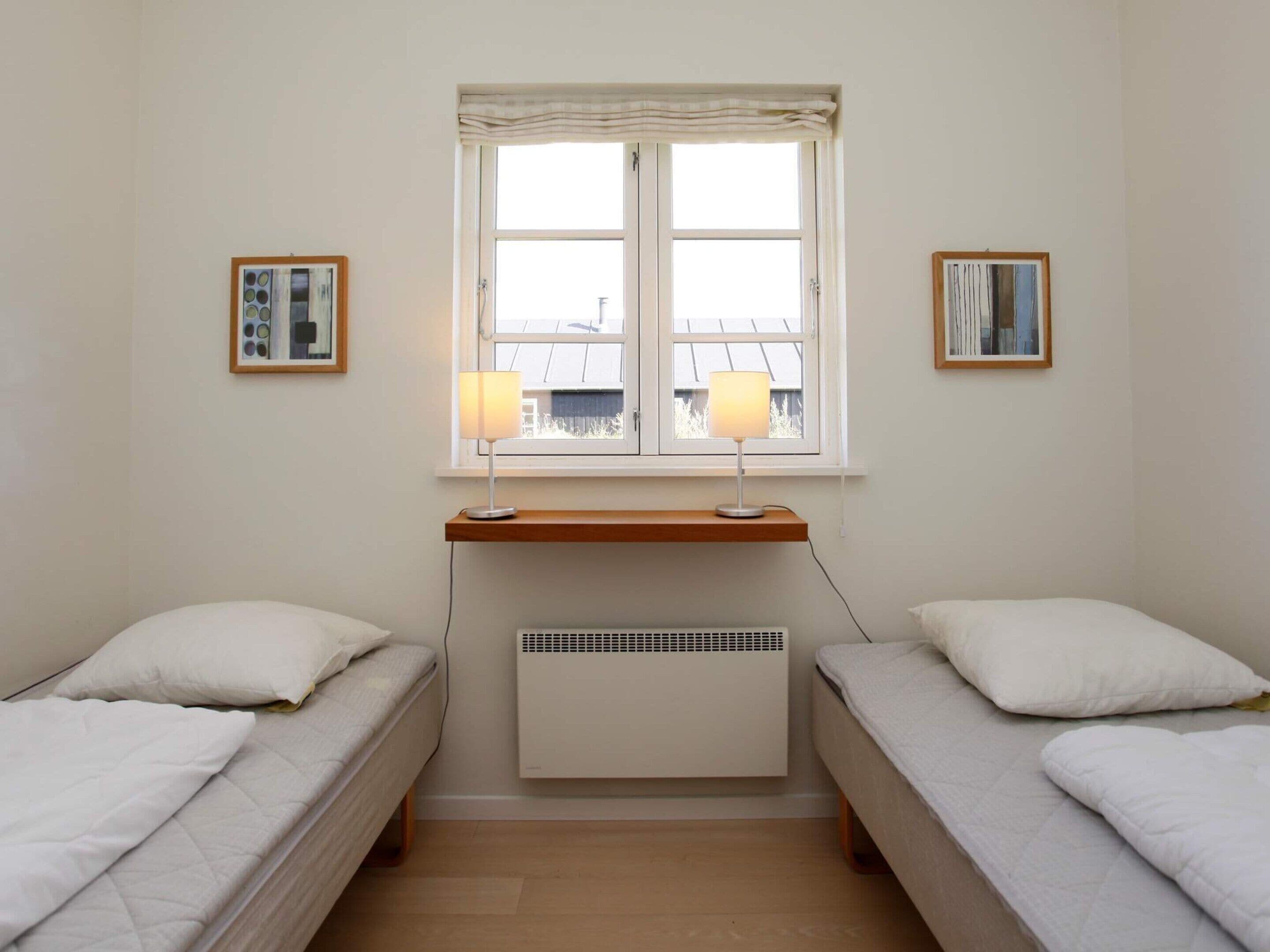 A bedroom with two single beds, a window with curtains, a radiator, and two framed pictures on the wall.