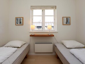 A bedroom with two single beds, a window with curtains, a radiator, and two framed pictures on the wall. - 5 Star Holiday Home in Nysted (Nysted)