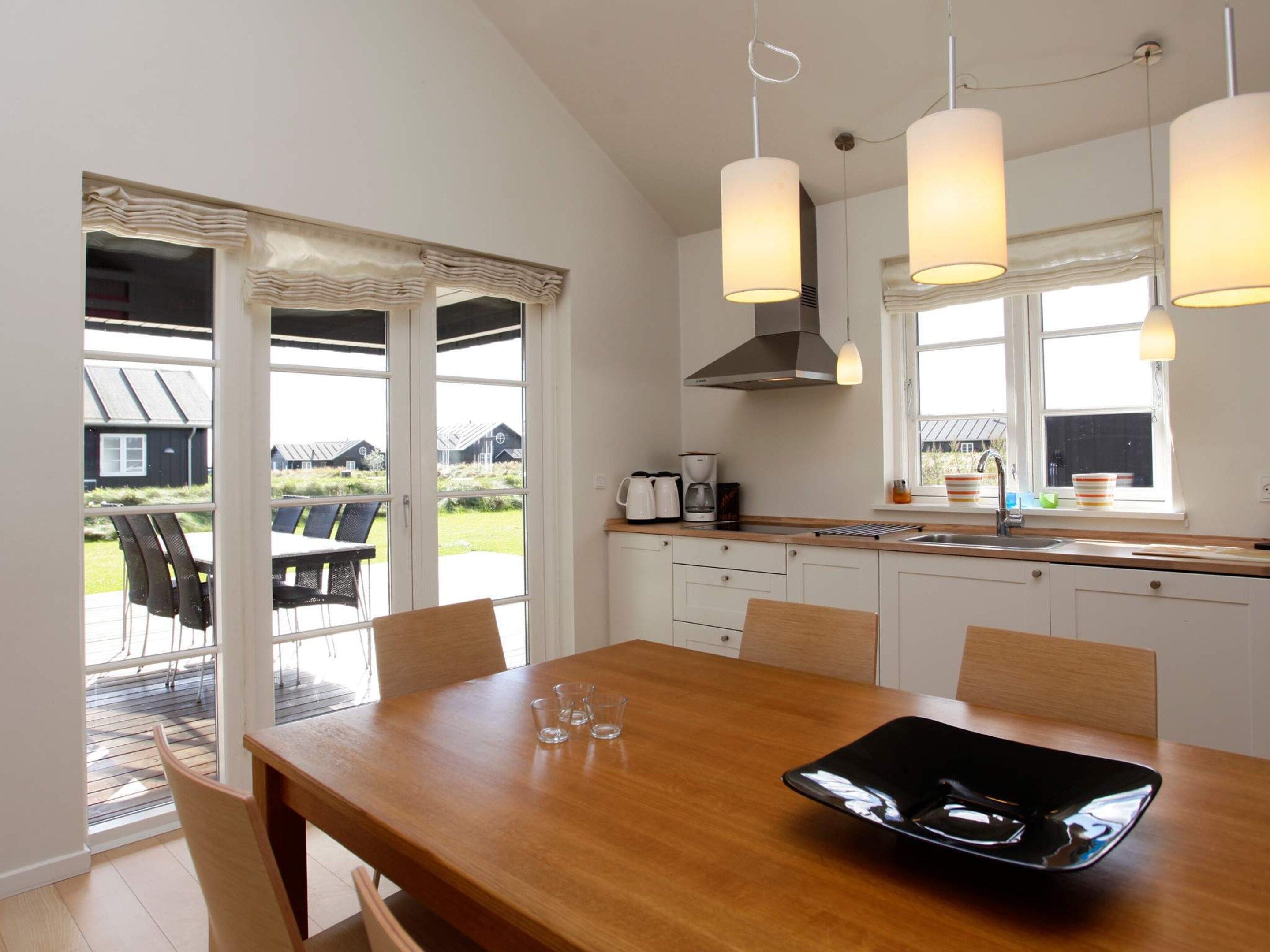 A modern kitchen with a dining area, large windows, and a view of the outdoors.