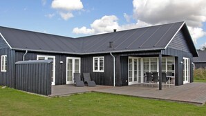 A modern house with a dark exterior, a covered patio with seating, and a large windowed area. - 5 Star Holiday Home in Nysted (Nysted)