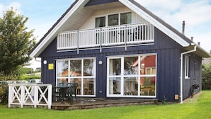 A two-story building with a balcony, large windows, and a deck area with outdoor furniture.
