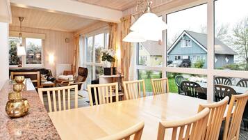 A spacious dining area with a large table and chairs, a kitchen area with a counter and appliances, and large windows offering a view of the outside.