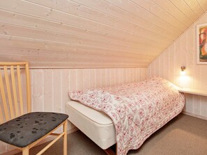 Une petite chambre avec un lit simple, un plafond en pente en bois et une chaise simple.