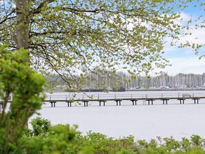 A waterfront view with a dock extending into calm water, surrounded by greenery and a row of sailboats in the background. - 8 Person Holiday Home in Gelting (Gelting)