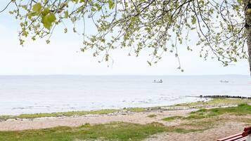 A beach with a path leading to a bench, a body of water, and a distant boat.