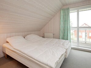A bedroom with a sloped ceiling, a large bed, a radiator, and a window with curtains. - 8 Person Holiday Home in Gelting (Gelting)