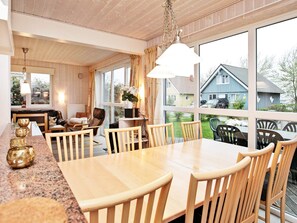 Un comedor amplio con una mesa y sillas grandes, una zona de cocina con mostrador y electrodomésticos, y ventanas grandes con vistas al exterior.