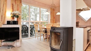 A cozy living room with a fireplace, a dining area with wooden furniture, and a large window offering a view of trees. - 8 Person Holiday Home in Gelting (Gelting)