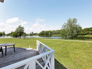 A wooden deck with a table and chairs, a white railing, and a view of a lake surrounded by trees.