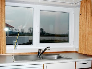 Eine Küche mit einem Doppelwaschbecken, einem Fenster mit Blick auf ein Gewässer und Bäume, sowie einer kleinen Vase mit einer Zahnbürste.