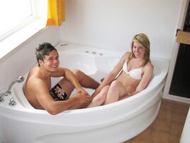 A bathtub with two people sitting inside, a window with curtains, and a door with a sign.